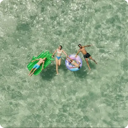 Vier Personen beim Baden und Spielen im Meer mit Luftmatratzen
